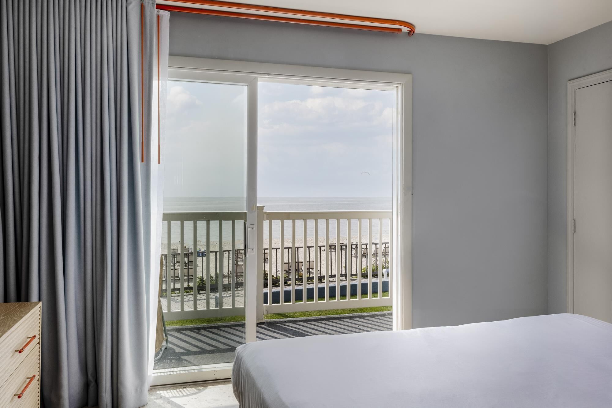 A hotel room with a bed, a sliding glass door to a balcony, and a view of the beach.