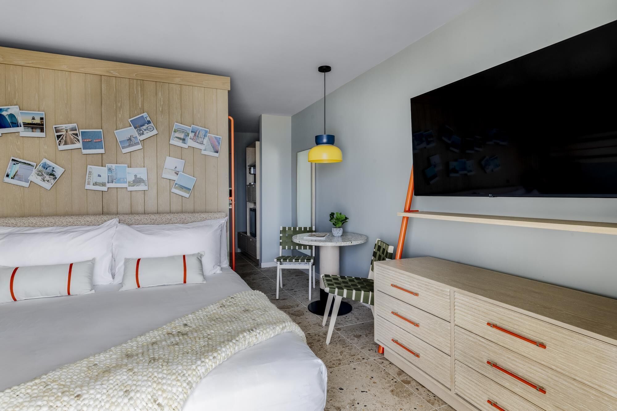 Une chambre à coucher avec un lit, une commode, un téléviseur et un mur décoré de photos.