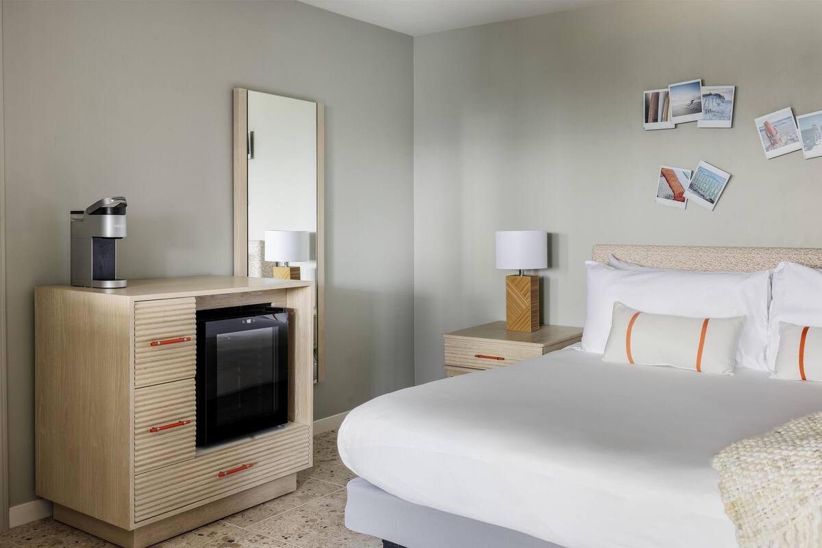 A hotel room with a bed, a dresser with a microwave, a nightstand with a lamp, and a wall with photos.