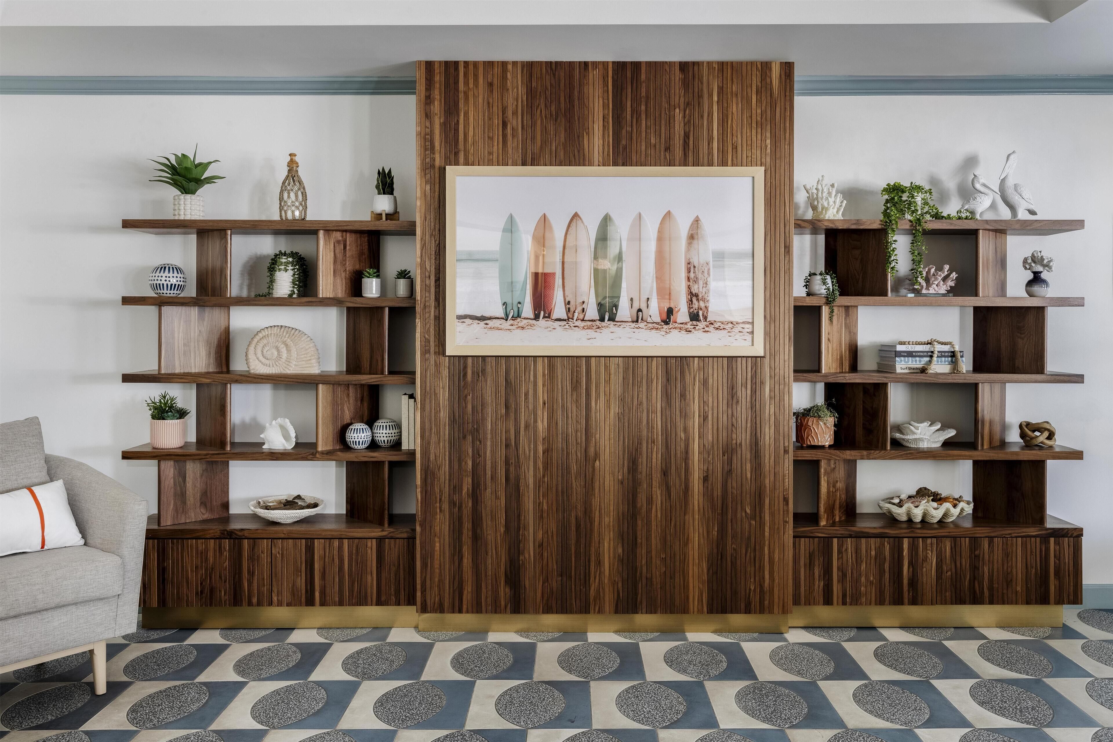 Un salon avec un mur d’accent en bois, une œuvre d’art représentant une planche de surf encadrée et des étagères ornées d’objets décoratifs.