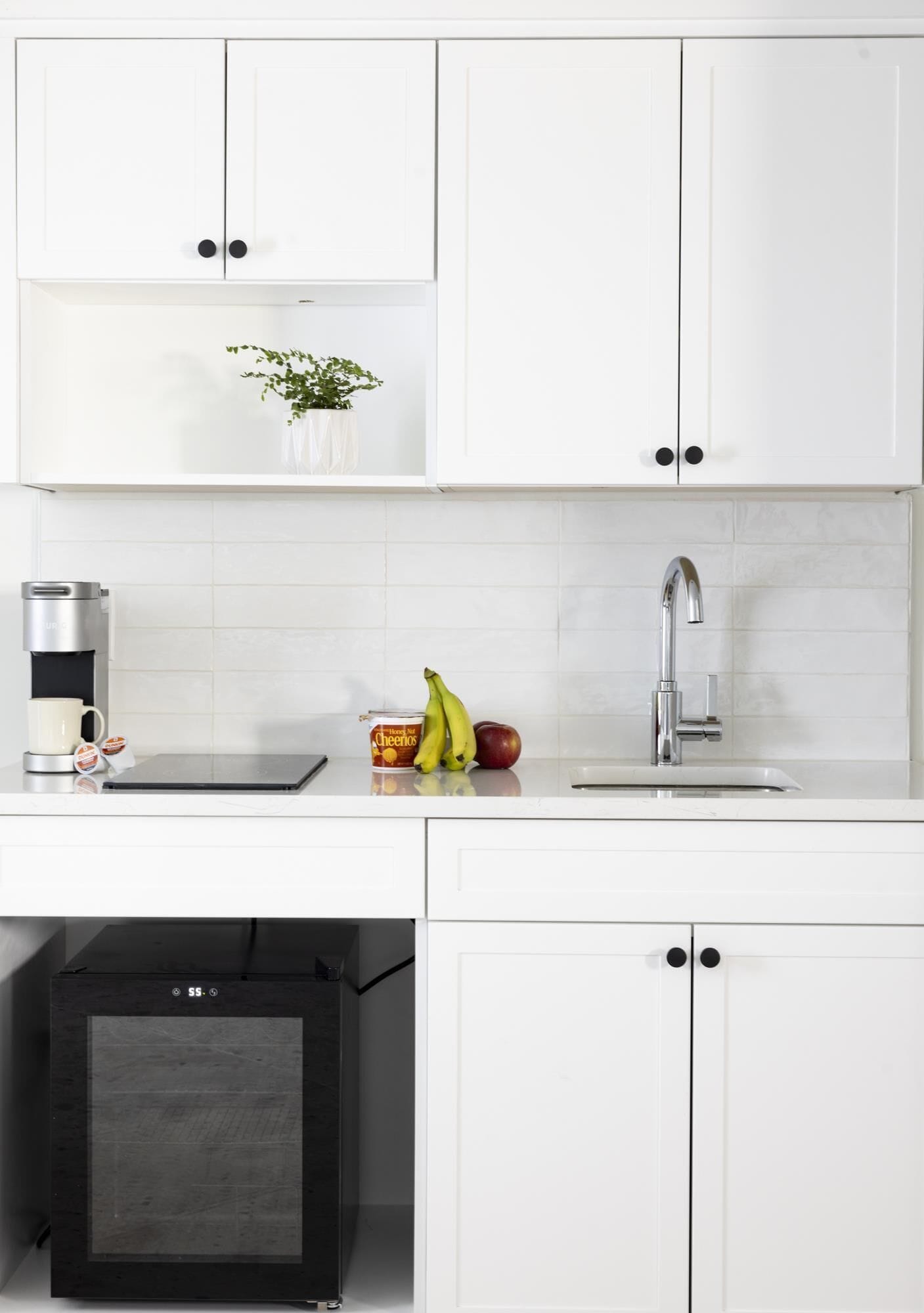 Una cocina moderna con armarios blancos, un lavamanos de acero inoxidable, una cafetera y una pequeña planta en la encimera.