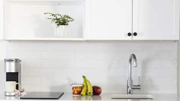 Una cocina moderna con armarios blancos, un lavamanos de acero inoxidable, una cafetera y una pequeña planta en la encimera.