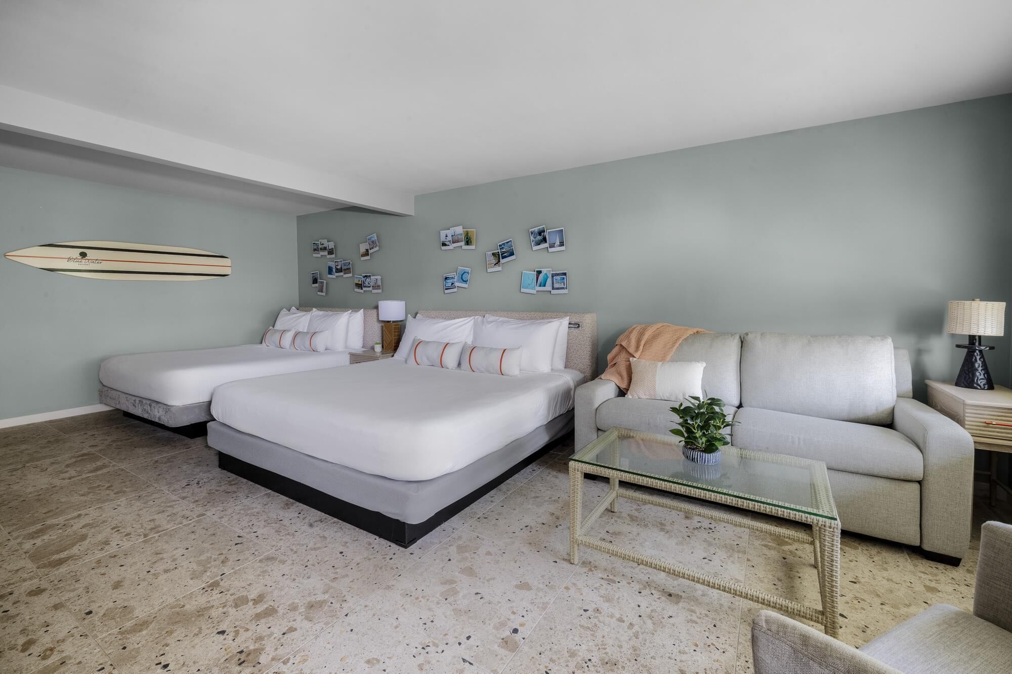 A hotel room with two beds, a sofa, a glass coffee table, and a wall decorated with photos.