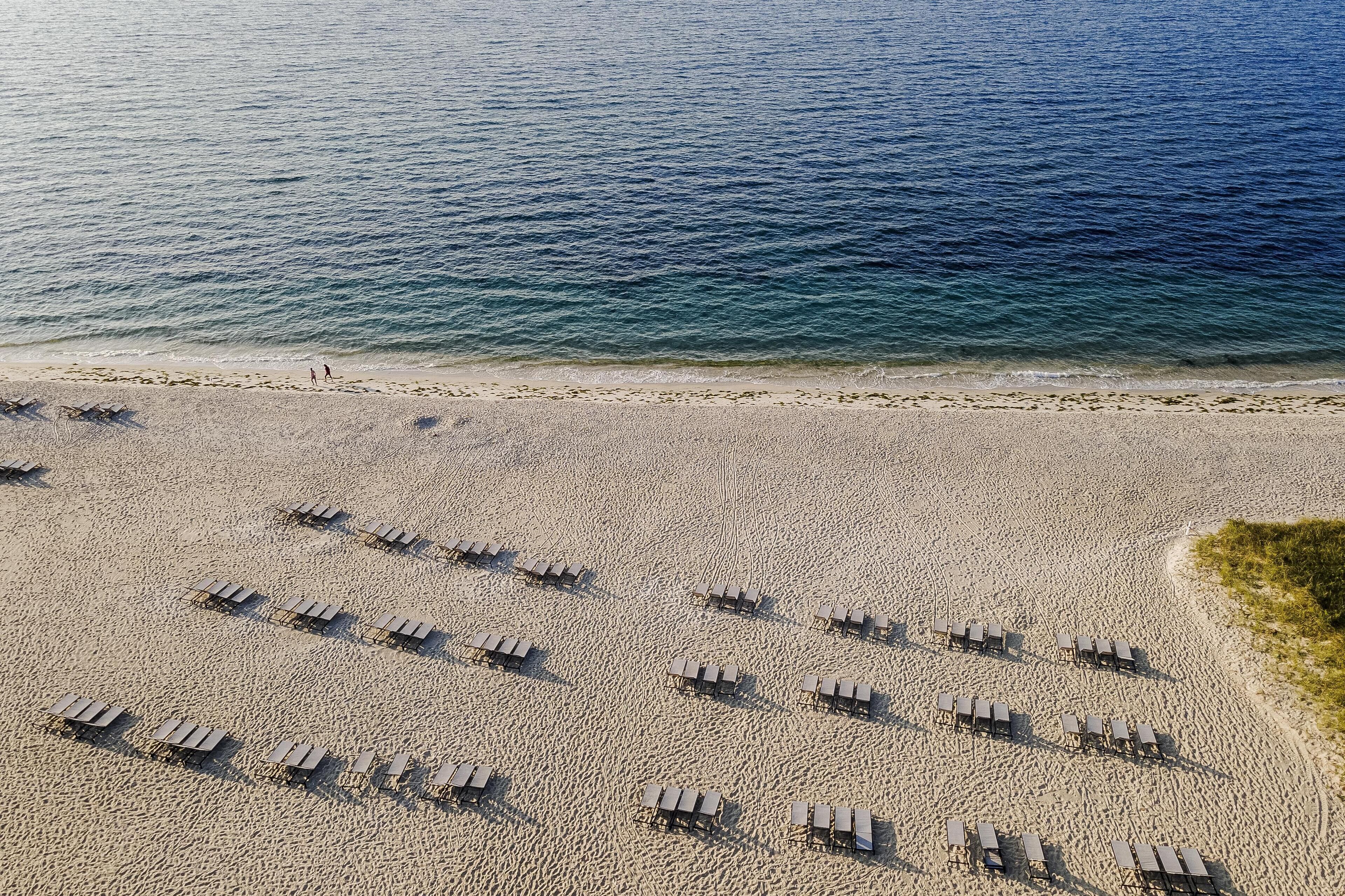Vue aérienne d’une plage où des rangées de chaises de plage et de parasols sont disposées selon un motif en grille.
