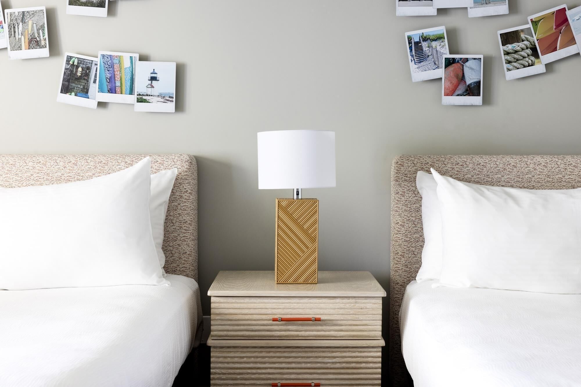 A hotel room with two beds, a nightstand with a lamp, and a wall decorated with photos.