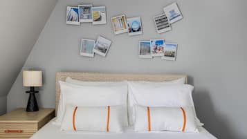 A neatly made bed with white bedding and orange-striped pillows, a bedside table with a lamp, and a wall adorned with various photographs.