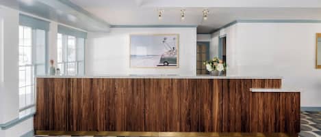A reception area with a wooden reception desk, a framed picture on the wall, and patterned floor tiles.