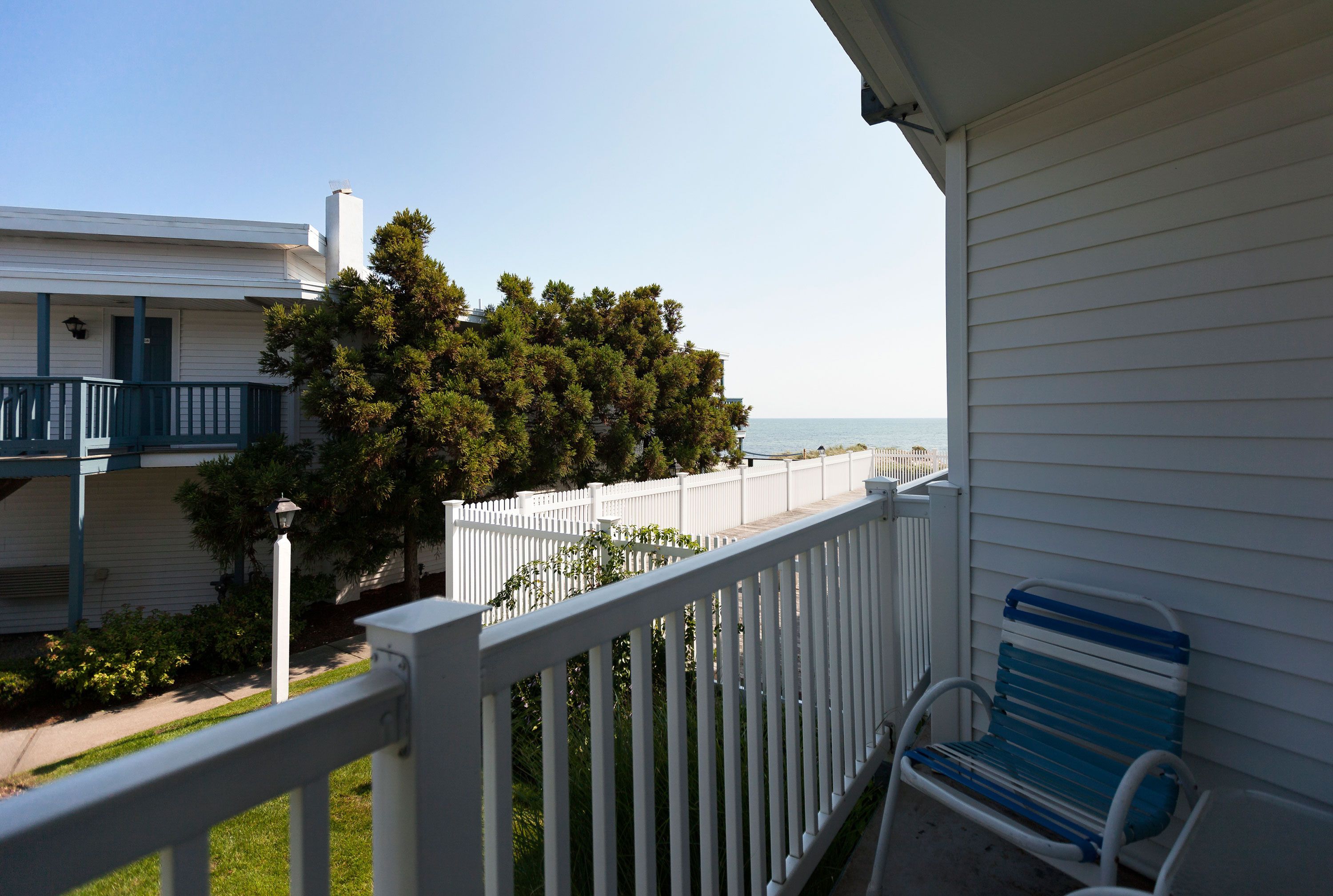 A balcony with a white railing, a blue and white bench, and a view of the sea.