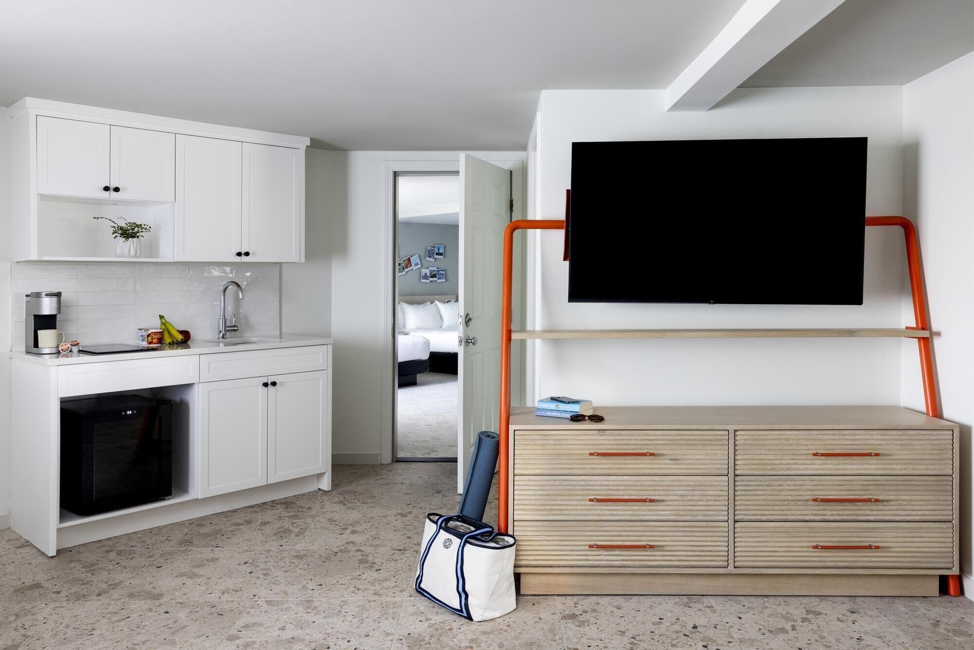A compact living space with a kitchenette, a bed, and a TV mounted on a wall.