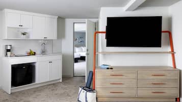 A compact living space with a kitchenette, a bed, and a TV mounted on a wall.