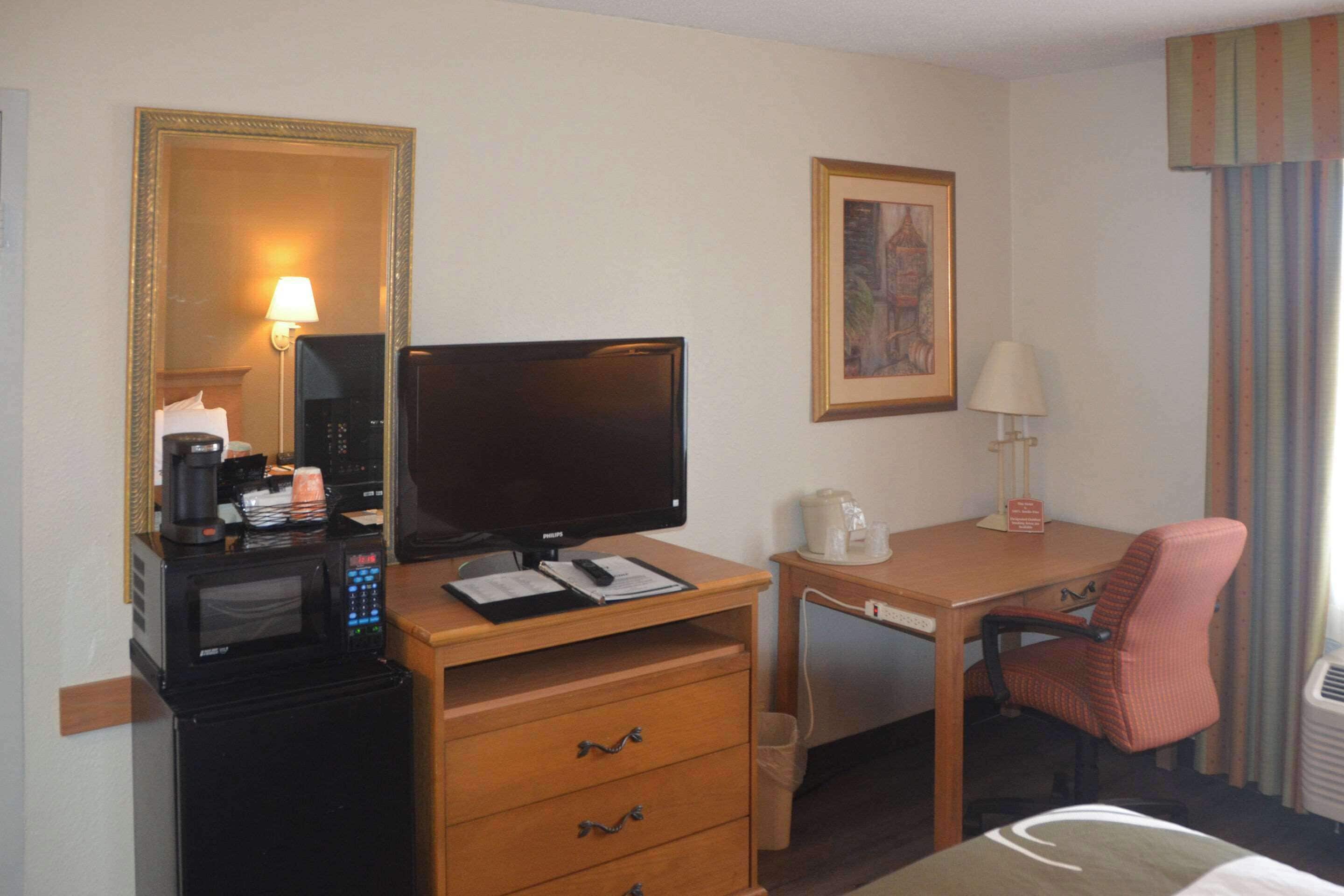 Une chambre d’hôtel équipée d’un bureau, d’une télévision, d’un four à micro-ondes, d’une chaise, d’une petite poubelle et d’un tableau encadré au mur.