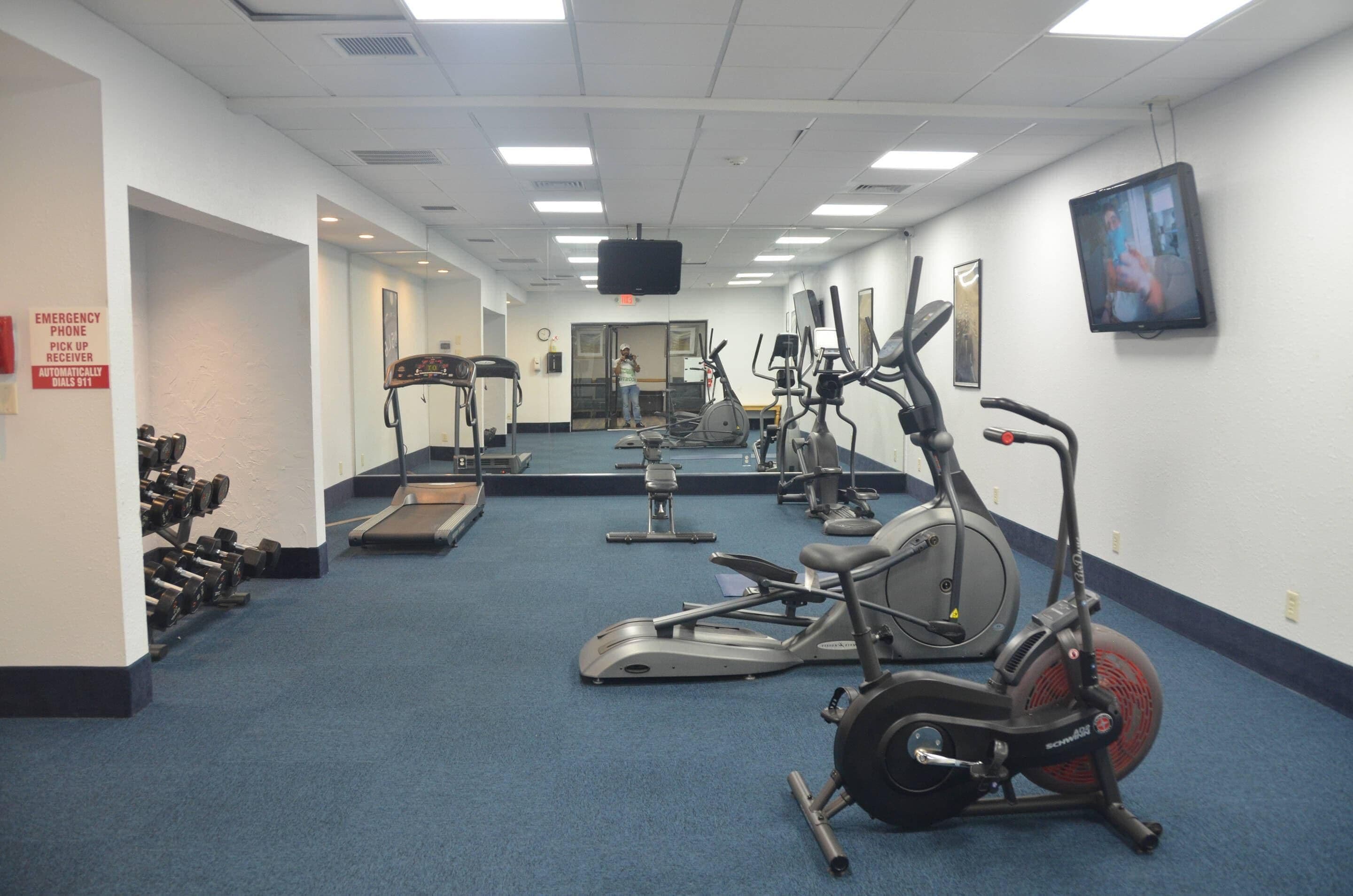 Un gimnasio con diversos equipos de ejercicio, incluyendo cintas de correr, elípticas y pesas libres.