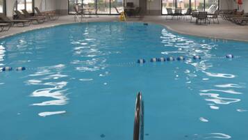 Una piscina interior con agua cristalina, separadores de carril y sillones de descanso alrededor del borde.