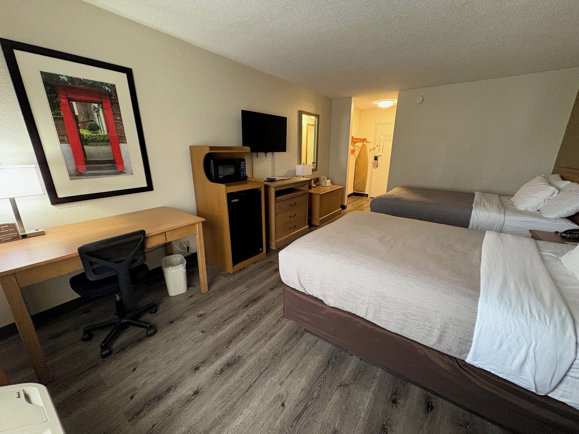 A hotel room with a bed, desk, chair, microwave, and a TV on the wall.