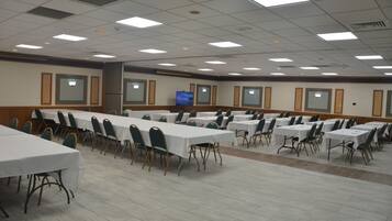 Uma sala de conferências com várias mesas e cadeiras, uma televisão e piso revestido com azulejos.