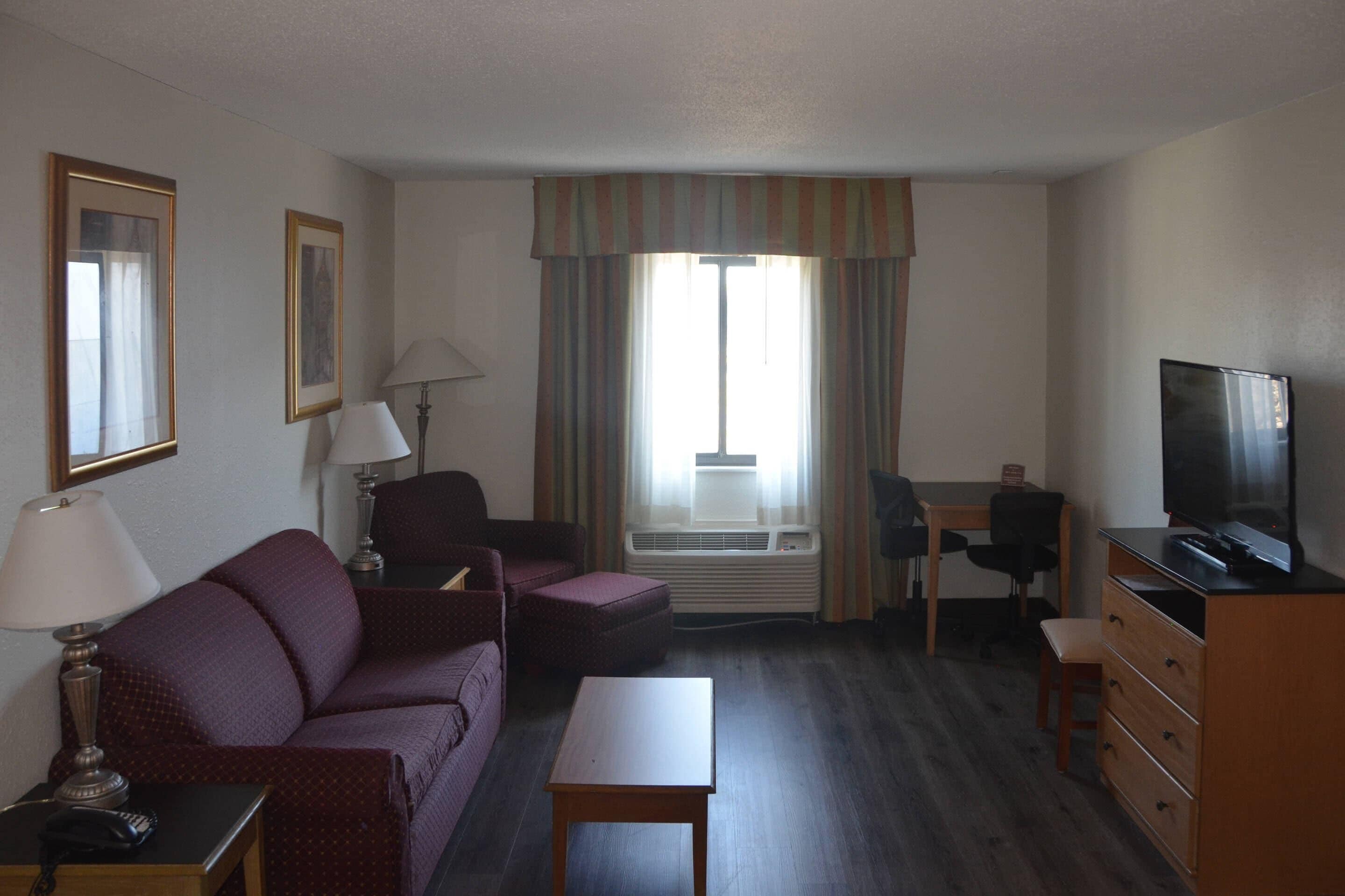 Une chambre d’hôtel équipée d’un canapé, d’une petite table, d’un bureau, d’une télévision et d’une fenêtre avec des rideaux.