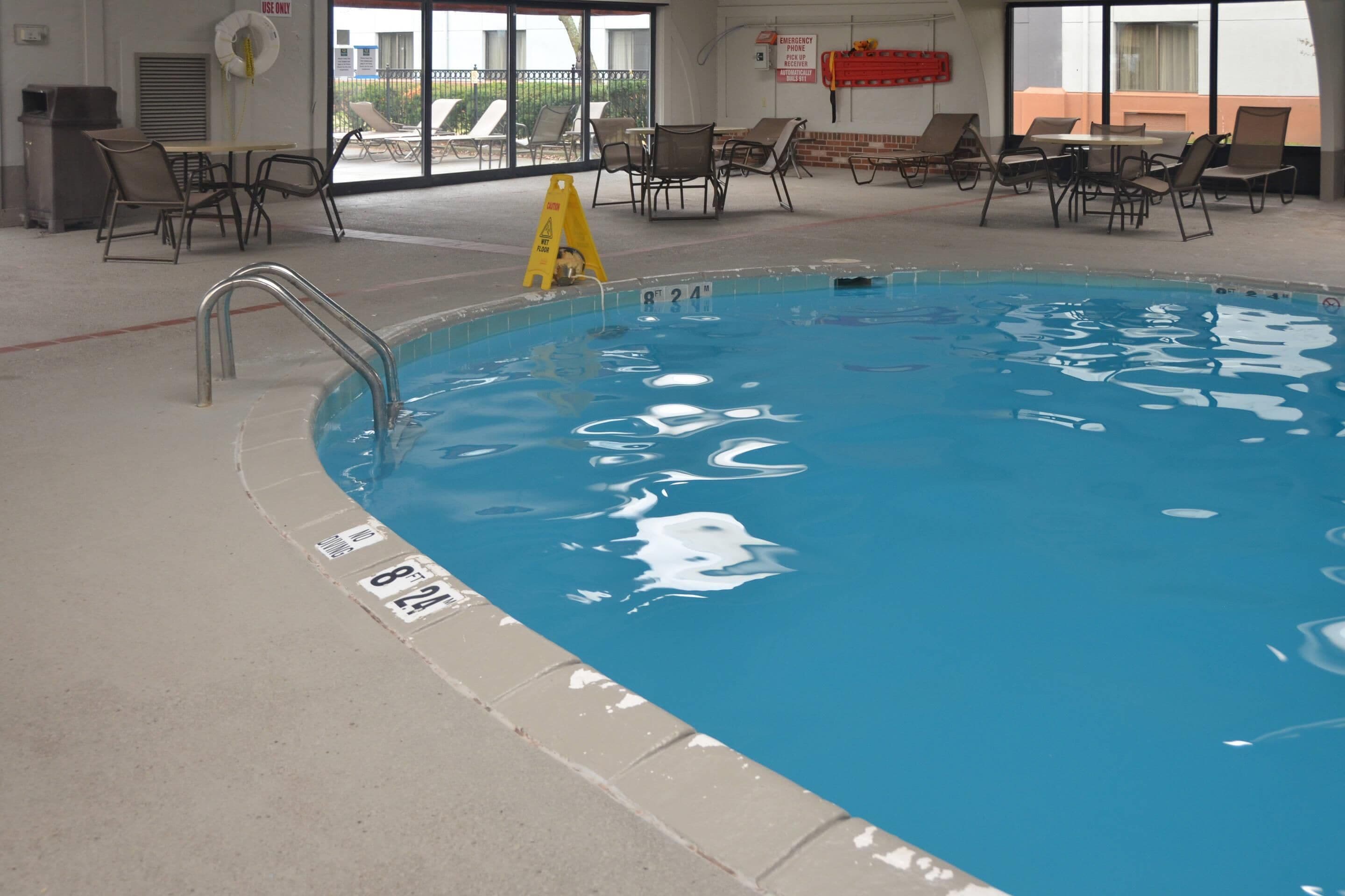 Piscina interna com água cristalina, cadeira de salva-vidas e espreguiçadeiras ao redor da área da piscina.