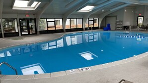 Una piscina interior con señalización clara, suelo de baldosas y techo con tragaluces.