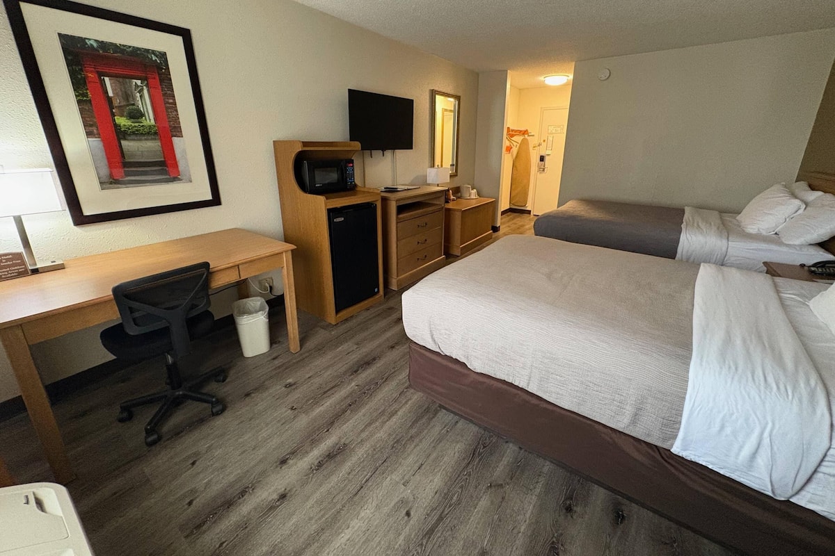 Quarto de hotel com cama, escrivaninha, cadeira, micro-ondas e televisão.
