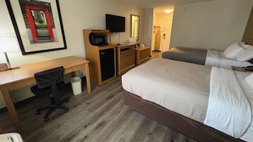 A hotel room with a bed, desk, chair, microwave, and a television.