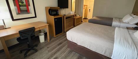 A hotel room with a bed, desk, chair, microwave, and a television.