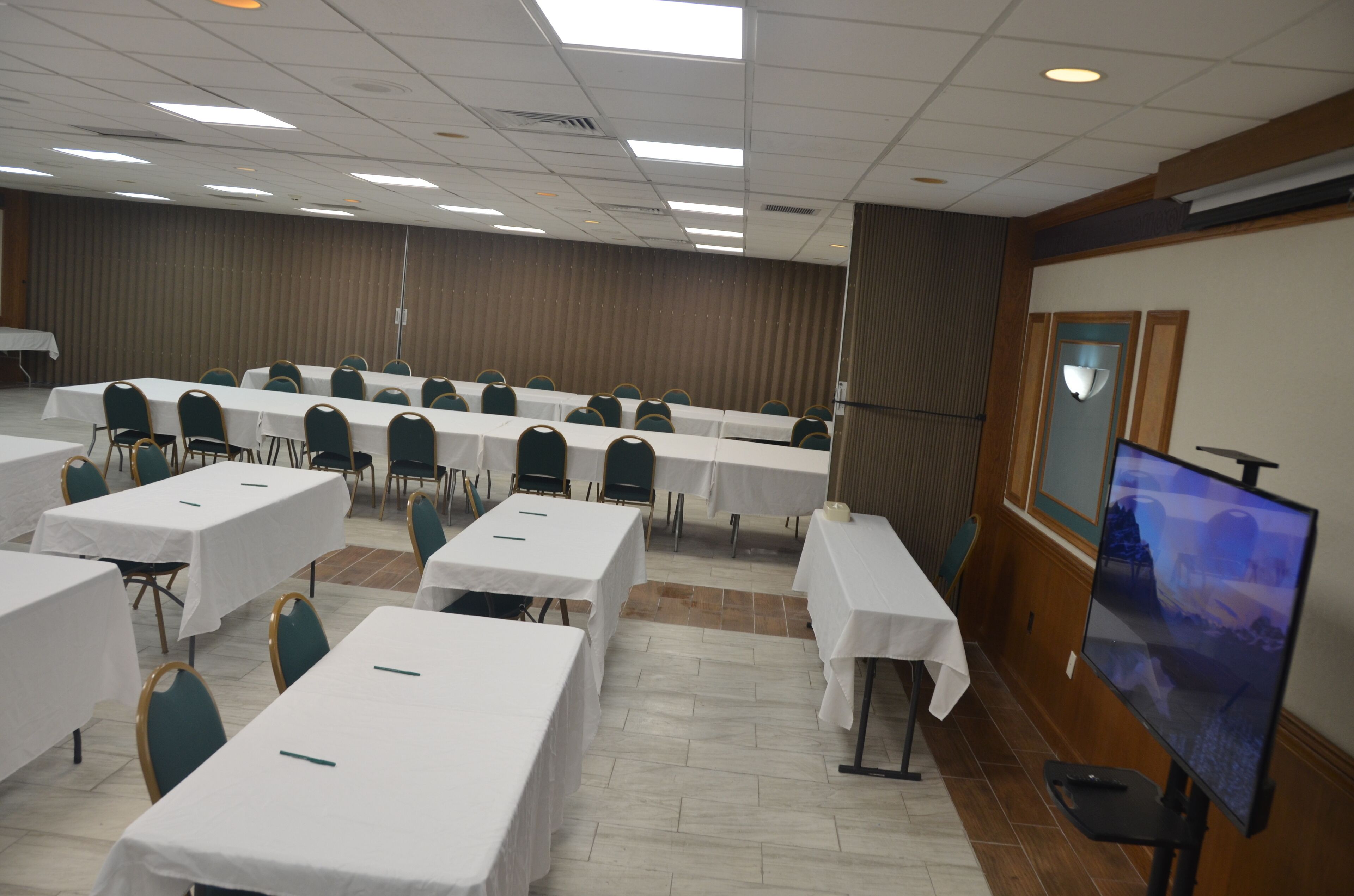 Une salle de conférence dotée de plusieurs tables et chaises, d’un grand écran et d’un mur décoratif en bois.