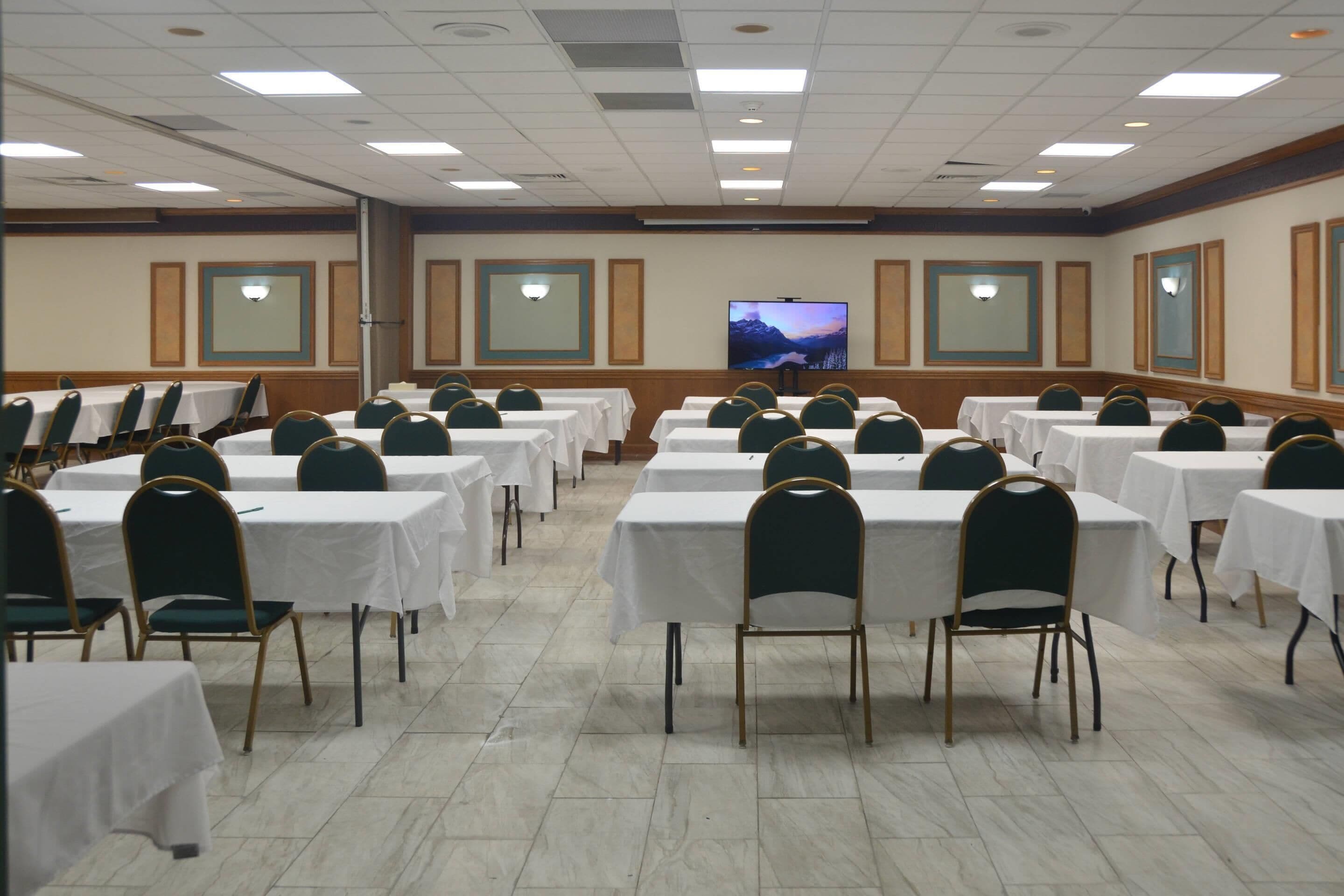 Un salón de conferencias con varias mesas y sillas, una pantalla grande y vistas a la montaña.
