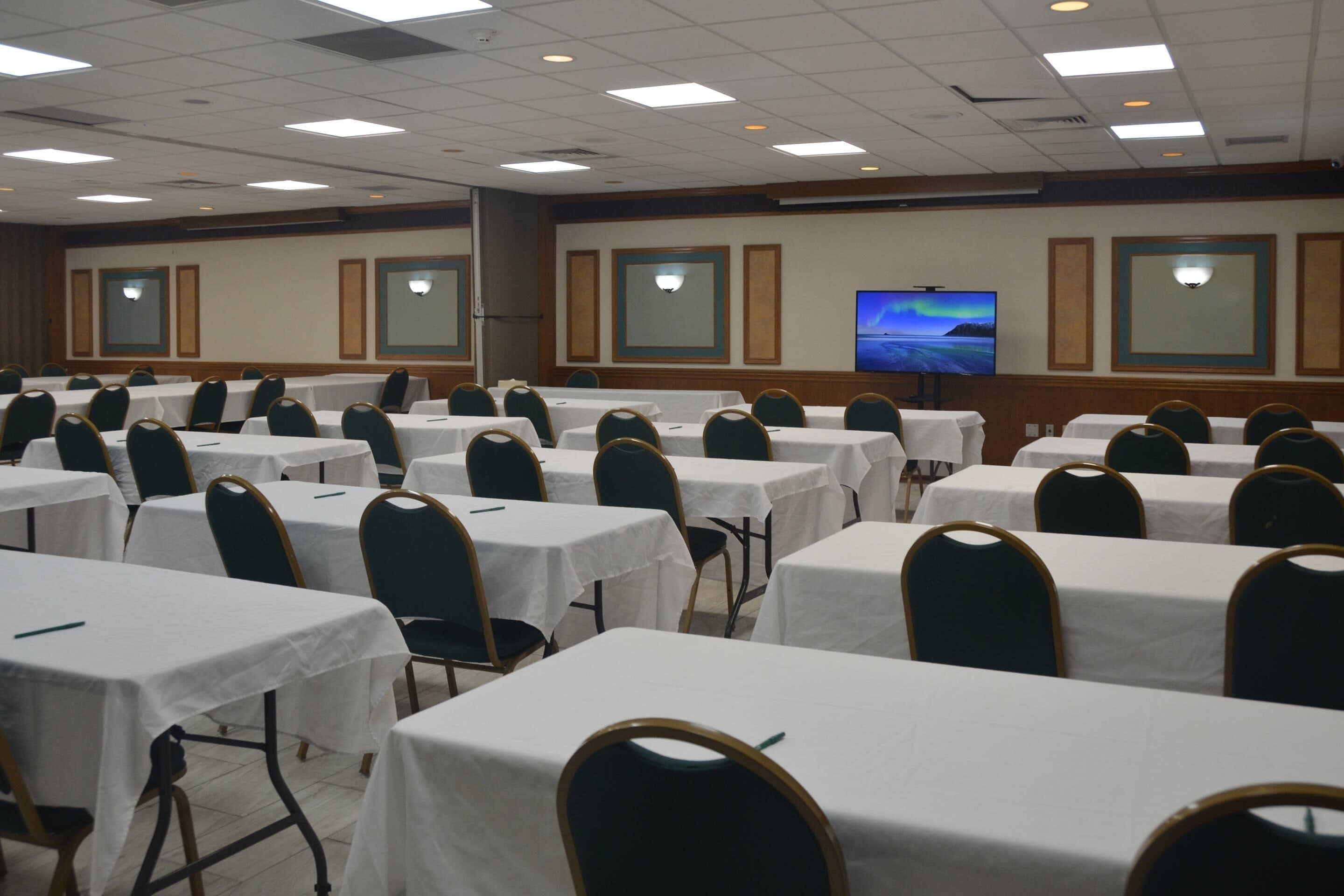 A conference room with multiple tables and chairs, a large screen, and a view of the night sky.