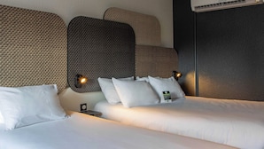 Ett hotellrum med två sängar, en väggmonterad luftkonditioneringsanläggning och ett nattduksbord med en lampa.