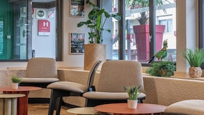 En hotellobby med bekväma sittplatser, en stor krukväxt och utsikt över omgivningarna.