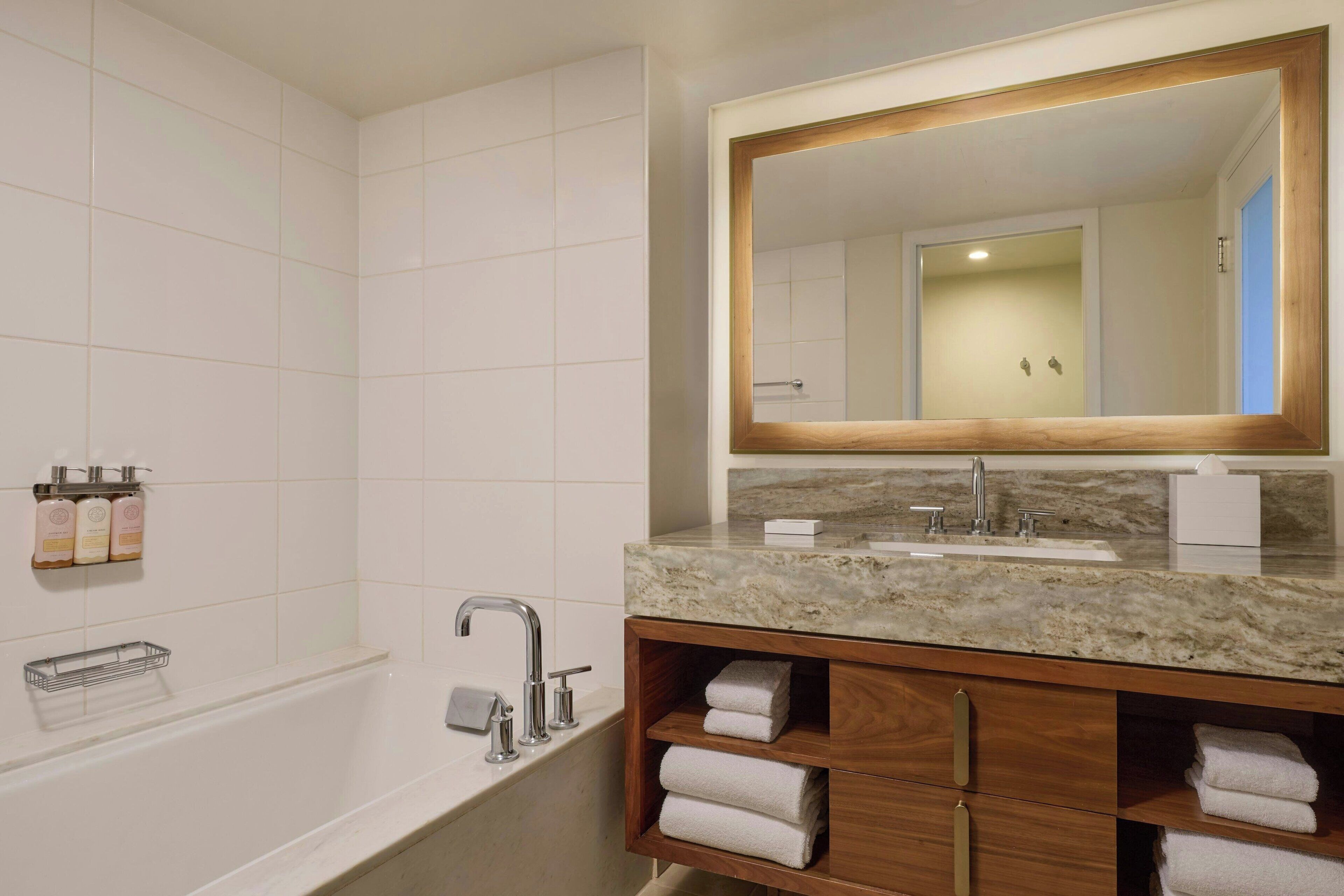 Un baño moderno con lavamanos de mármol, tocador de madera y un espejo grande.