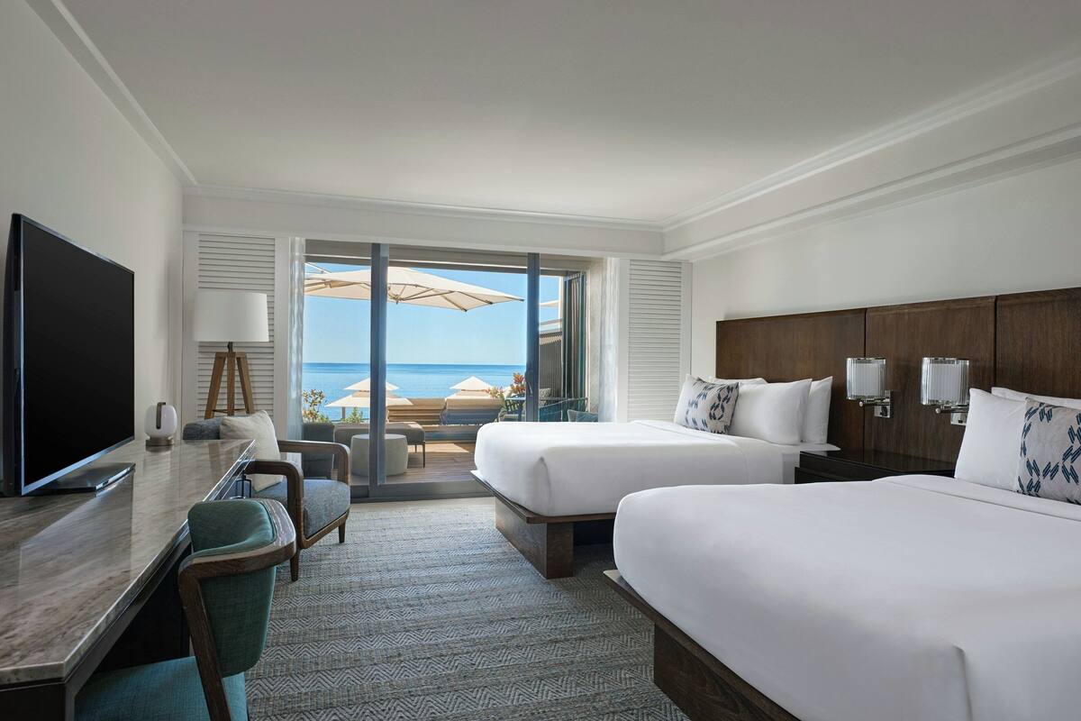 Une chambre d’hôtel avec deux lits, un bureau avec une télévision et une vue sur la plage.