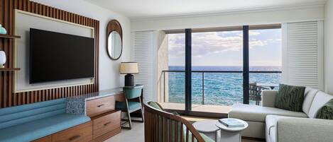 Un salon moderne doté d’un grand téléviseur, de sièges confortables, d’une vue sur l’océan et d’un balcon avec une balustrade.
