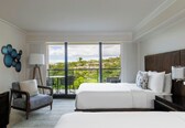 A hotel room with a large bed, a chair, a table, and a balcony with a view.