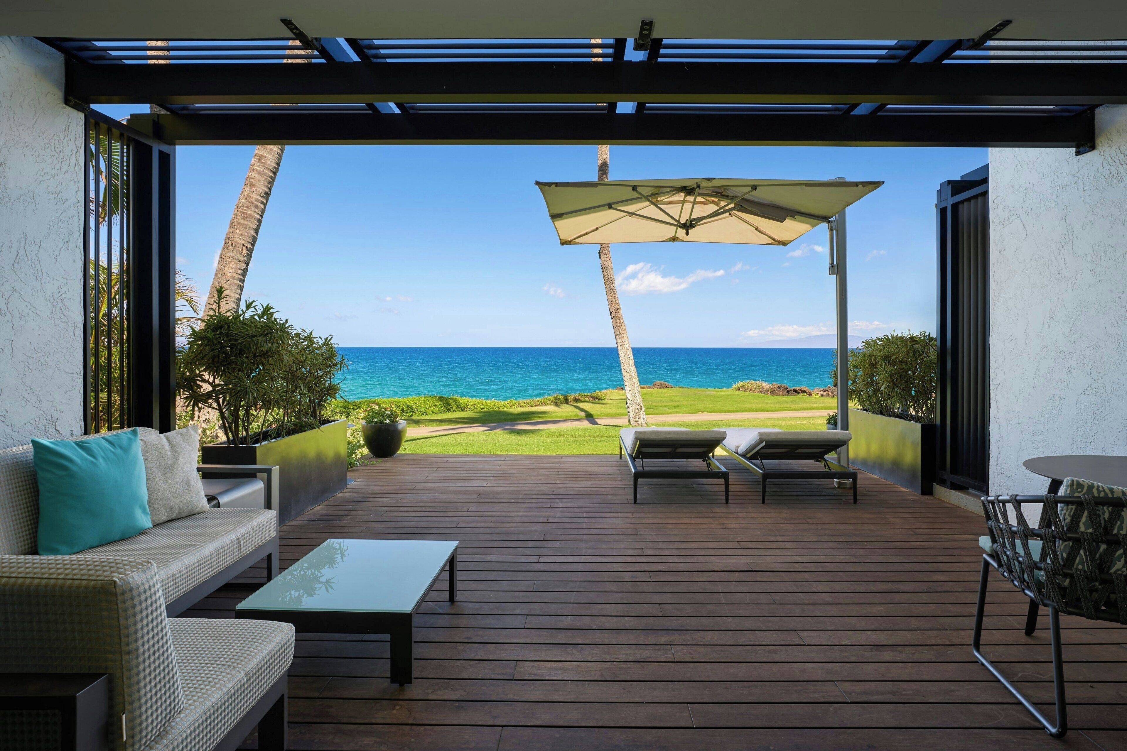 Una terraza de madera con sofá, sillas y una mesa, con vistas a una playa y un campo de golf.