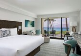 A hotel room with a large bed, a seating area with a view of the ocean, and a dining area with a view of the ocean.