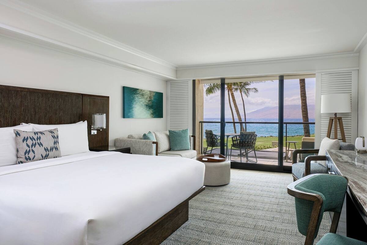 A hotel room with a large bed, a seating area with a view of the ocean, and a dining area with a view of the ocean.