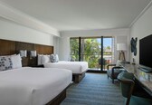 A hotel room with two beds, a desk, a TV, and a view of palm trees.