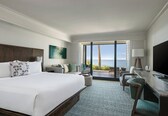 A hotel room with a large bed, a desk with a chair, a TV, and a view of the ocean.