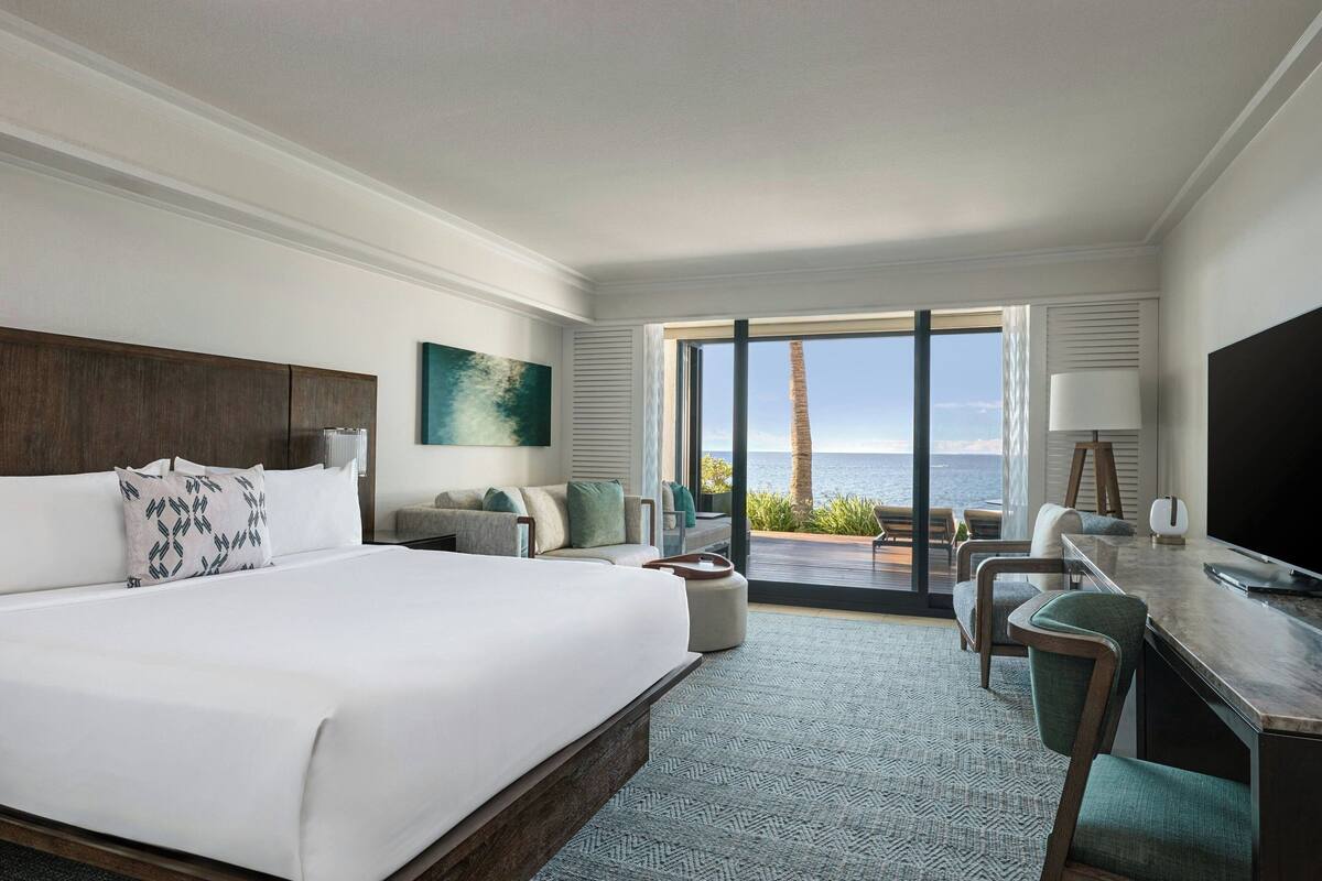 Une chambre d’hôtel avec un grand lit, un bureau avec une chaise, une télévision et une vue sur l’océan.