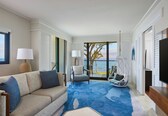 A modern living room with a sofa, chairs, a large window with a view, and a flat-screen TV.