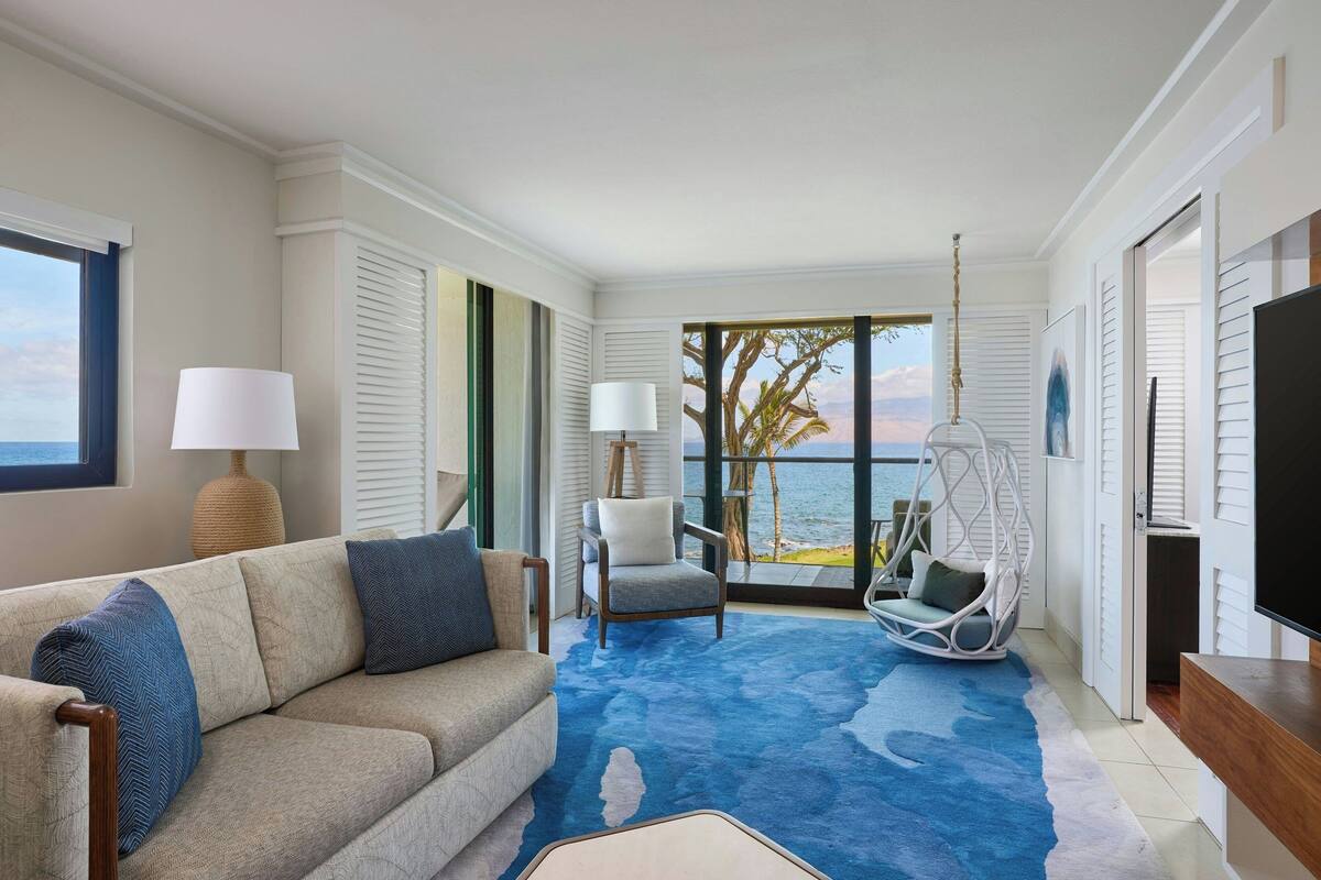 A modern living room with a sofa, chairs, a large window with a view, and a flat-screen TV.