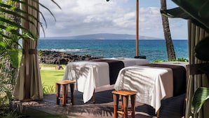 A serene outdoor seating area with two tables covered in white tablecloths and wooden stools, overlooking a coastal view with the ocean and a distant island. - Wailea Beach Resort - Marriott, Maui (Kihei)