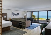 A hotel room with a bed, a sofa, a desk, and a view of the ocean.