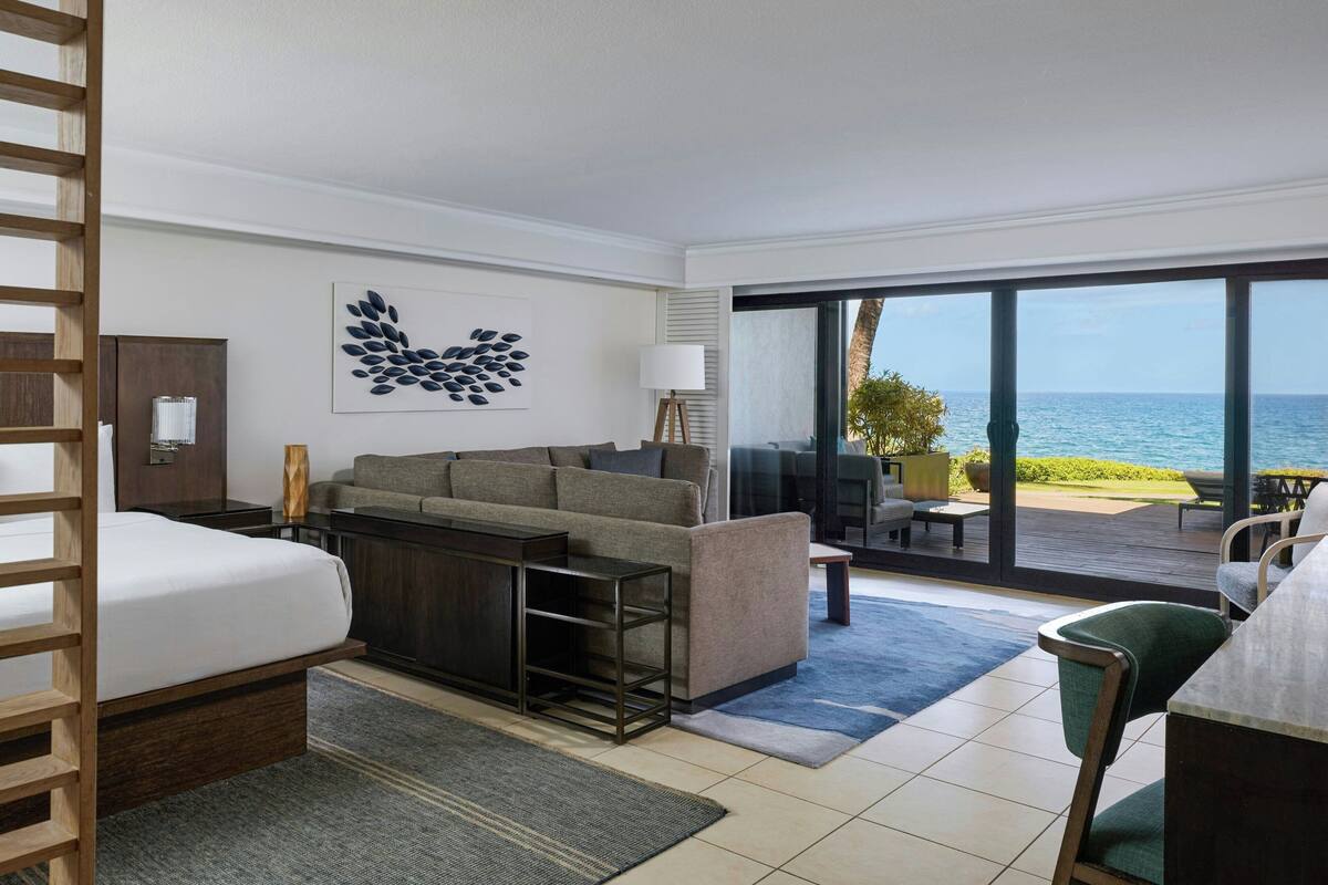 Une chambre d’hôtel avec un lit, un canapé, un bureau et une vue sur l’océan.