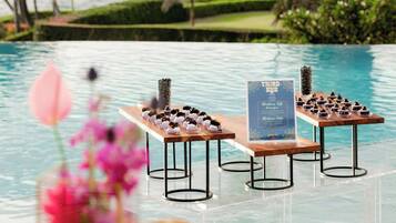 A poolside area with a table set for a meal, a sign indicating a menu, and a view of the ocean and palm trees.