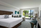 A hotel room with a large bed, a desk, a chair, a TV, and a view of the outdoors.