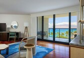 A hotel room with a large balcony, a TV, a desk, and a chair.