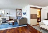 A modern hotel room with a sofa, armchair, and a small coffee table. There is a wooden floor and a blue rug.
