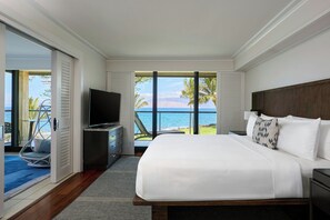 A bedroom with a large bed, a TV, and a view of the ocean.